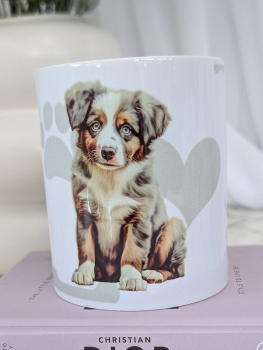 White ceramic dishwasher proof mug with watercolour style image of Australian Shepherd puppy against a background of soft grey hearts, pawprints and bones