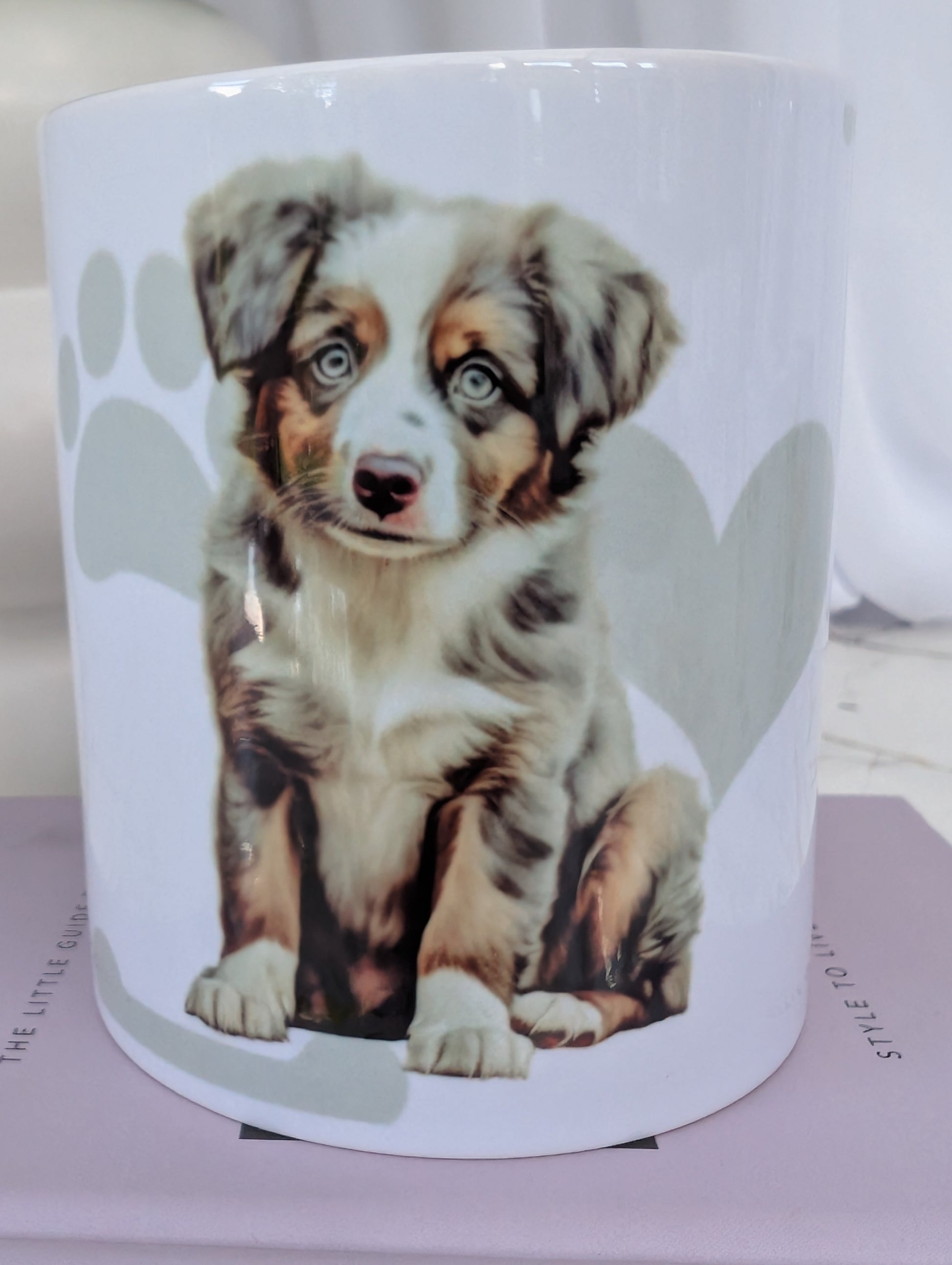 Close up white ceramic dishwasher proof mug with watercolour style image of Australian Shepherd puppy against a background of soft grey hearts, pawprints and bones