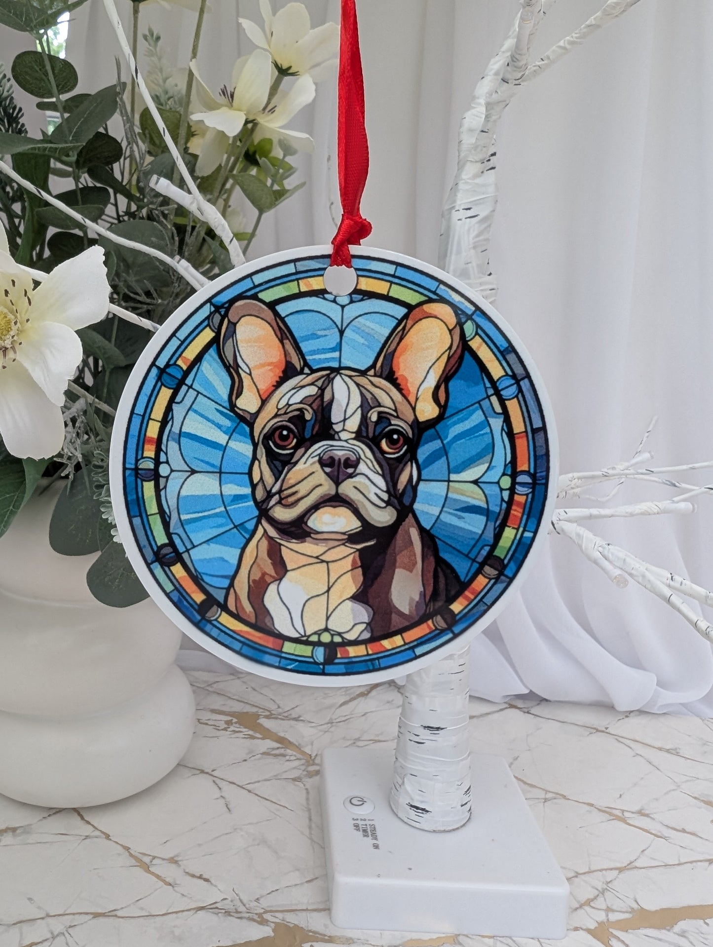 Round, aluminium, stained glass style French bulldog hanging ornament hanging on a white tree branch 
