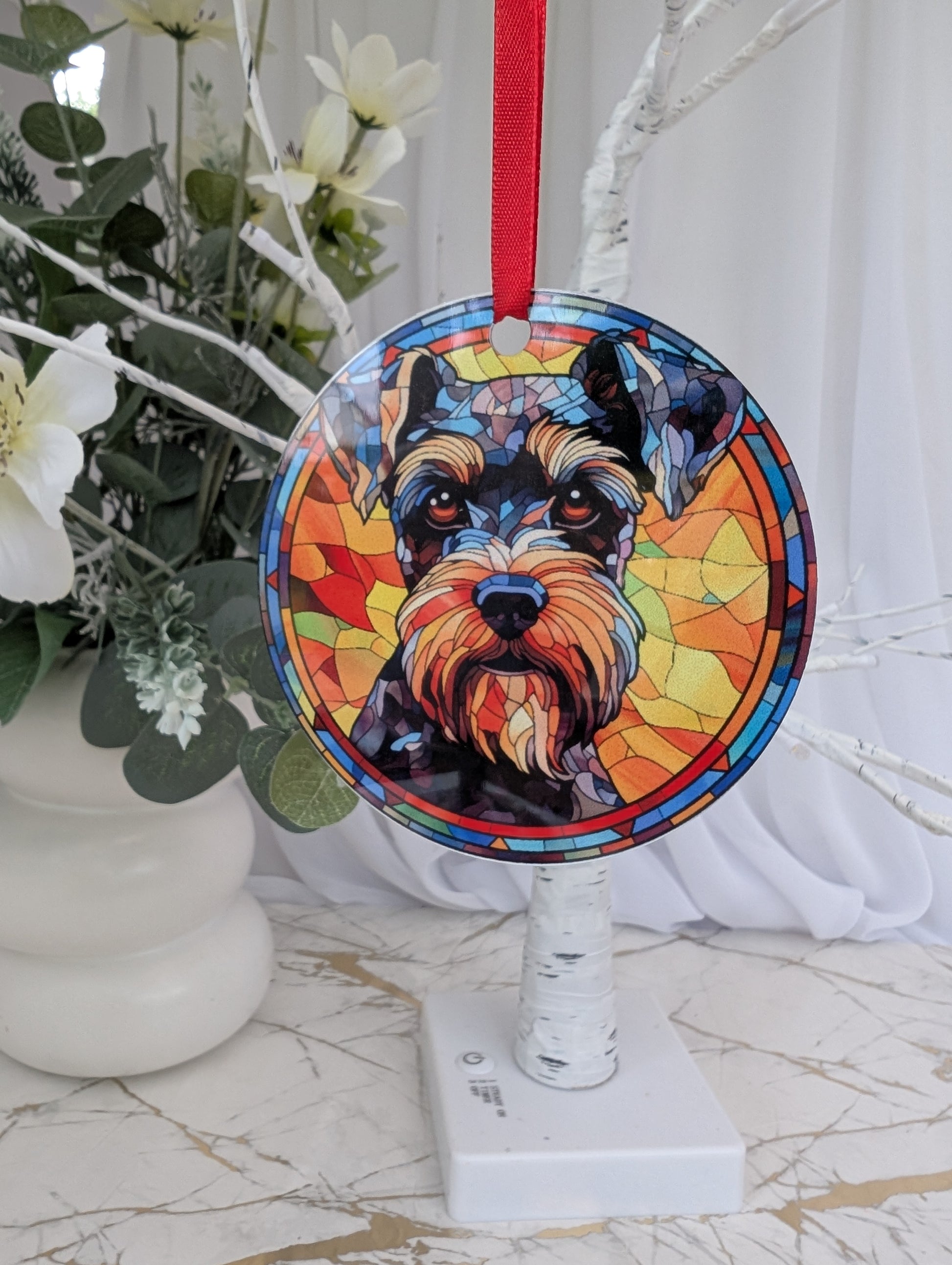 Lightweight aluminium, multicolour, 9cm round Schauzer dog hanging ornament in stained glass style with red ribbon hanging from a tree
