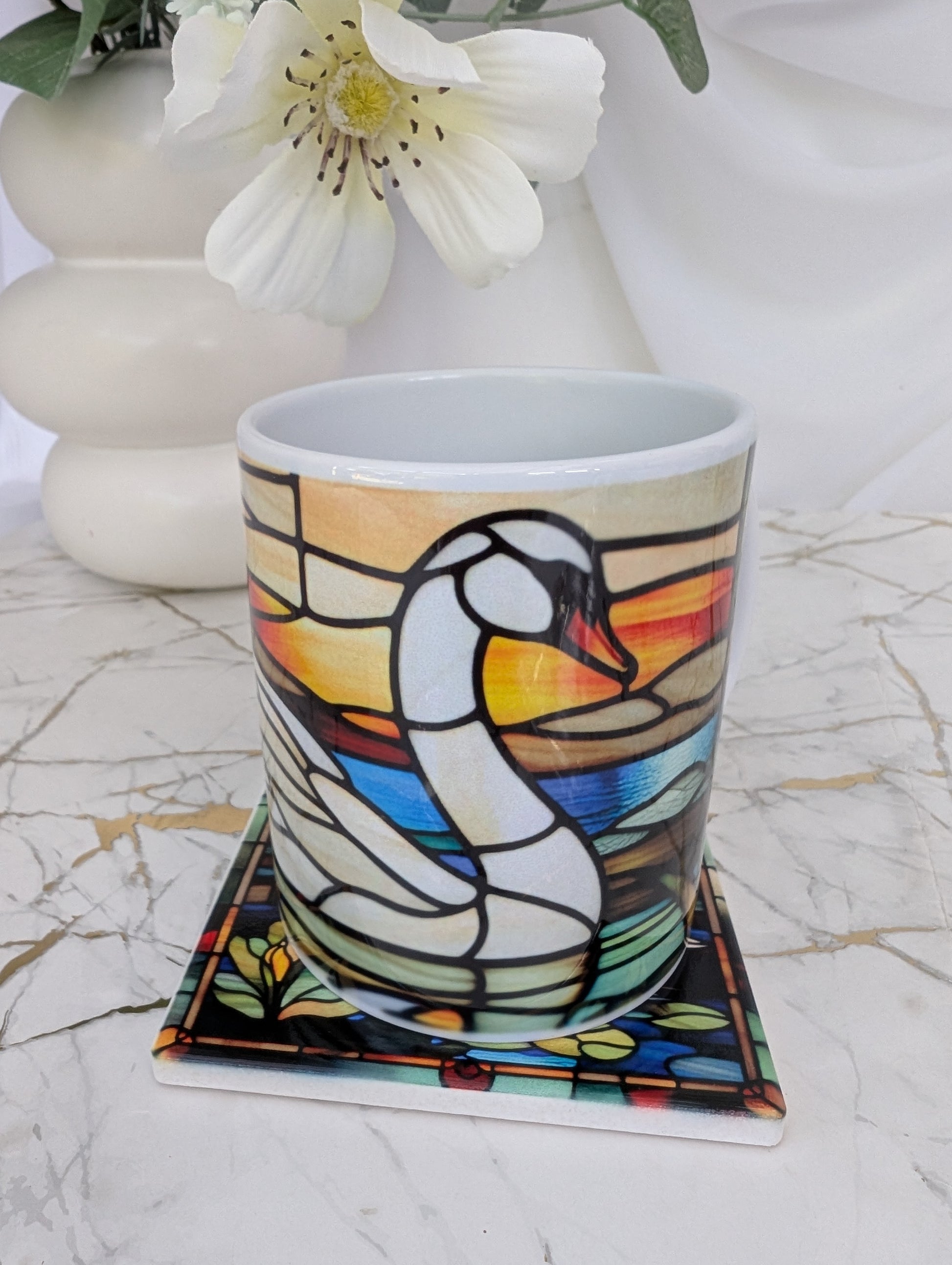 front view of  a square swan stained glass effect  mug on top of a ceramic coaster 