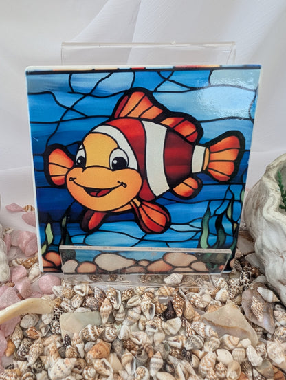 Stained glass panel of a clownfish on a white background with seashells below.