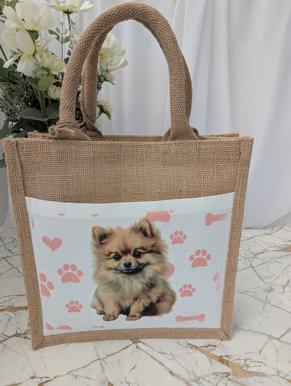 Front view of eco friendly jute tote bag with cream front pocket printed with Pomeranian dog and background of pink pawprint, hearts and bones