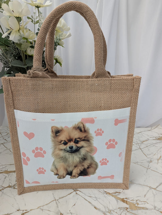 Front view of eco friendly jute tote bag with cream front pocket printed with Pomeranian dog and background of pink pawprint, hearts and bones