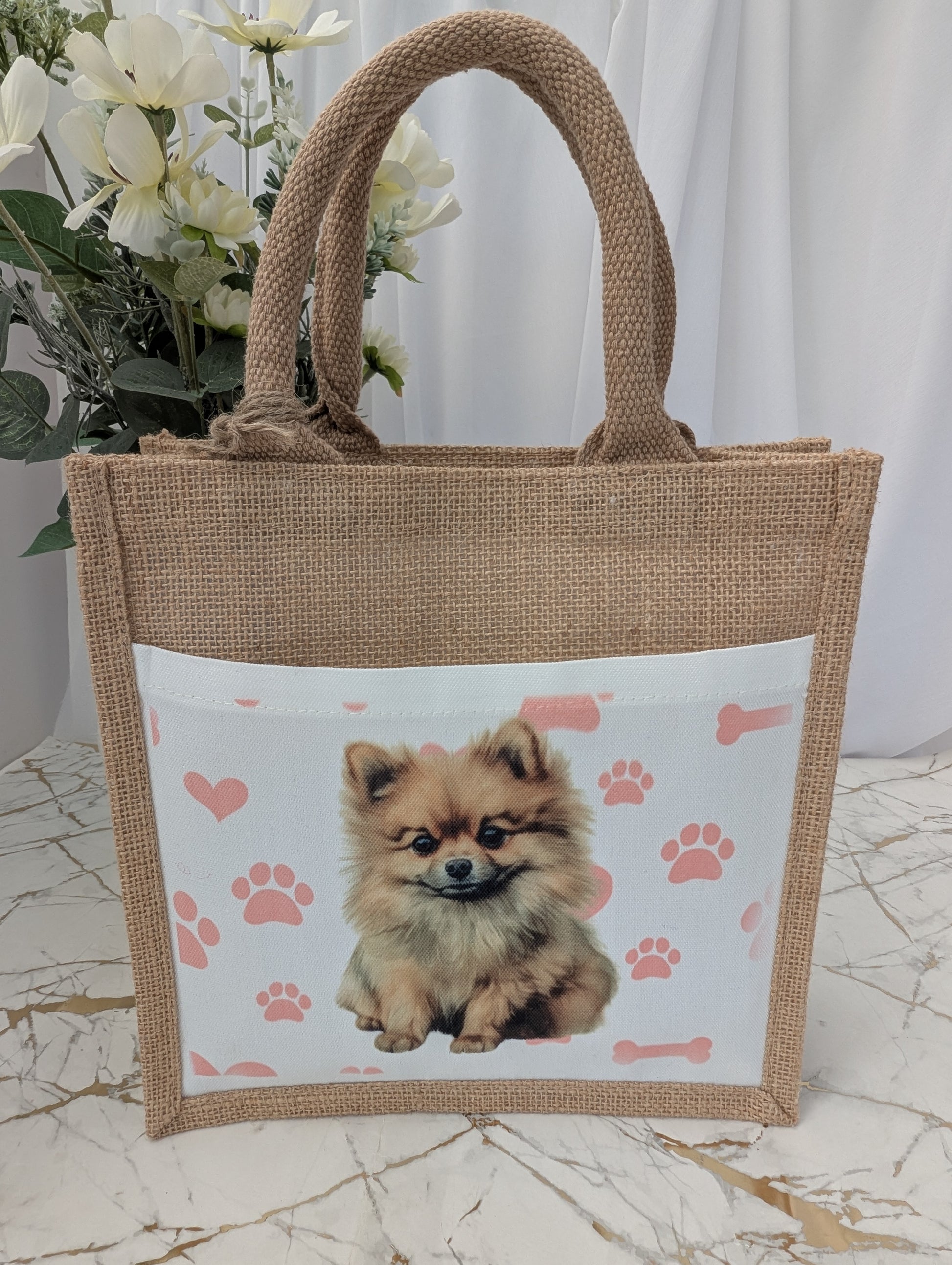 Eco friendly jute tote bag with cream front pocket printed with Pomeranian dog and background of pink pawprint, hearts and bones