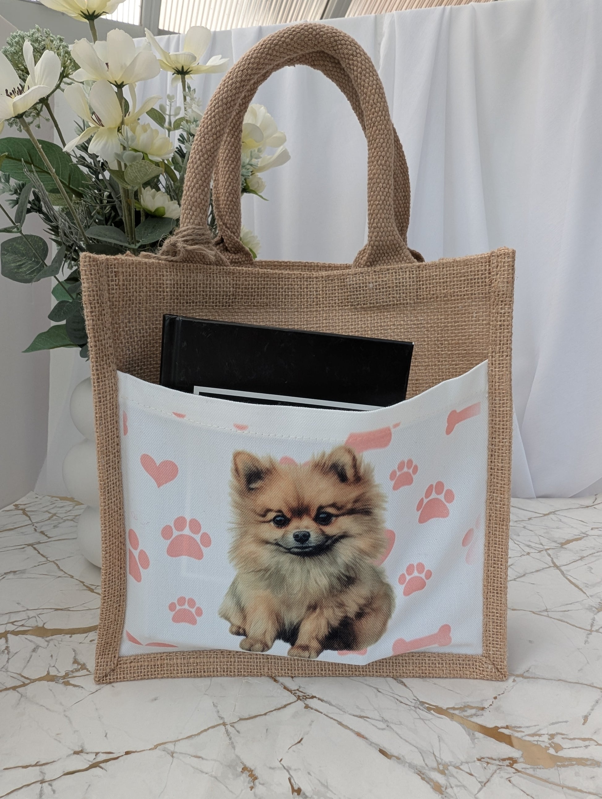  eco friendly jute tote bag with cream front pocket printed with Pomeranian dog and background of pink pawprint, hearts and bones - showing book in the pocket