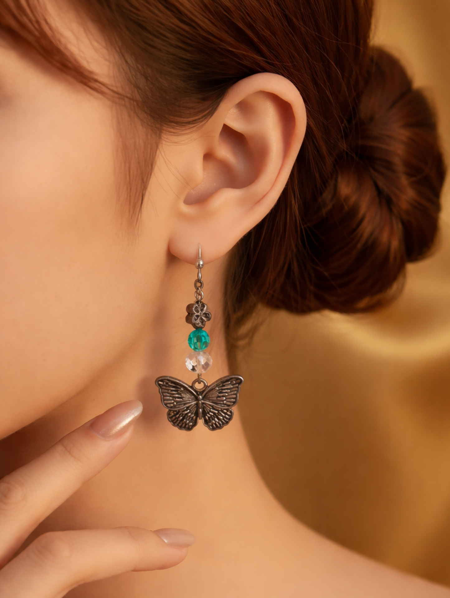 Butterfly earrings with a green gemstone worn by a model against a gold background