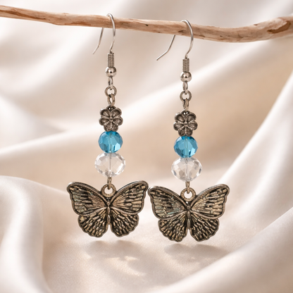 Butterfly earrings with blue and clear beads on a beige background