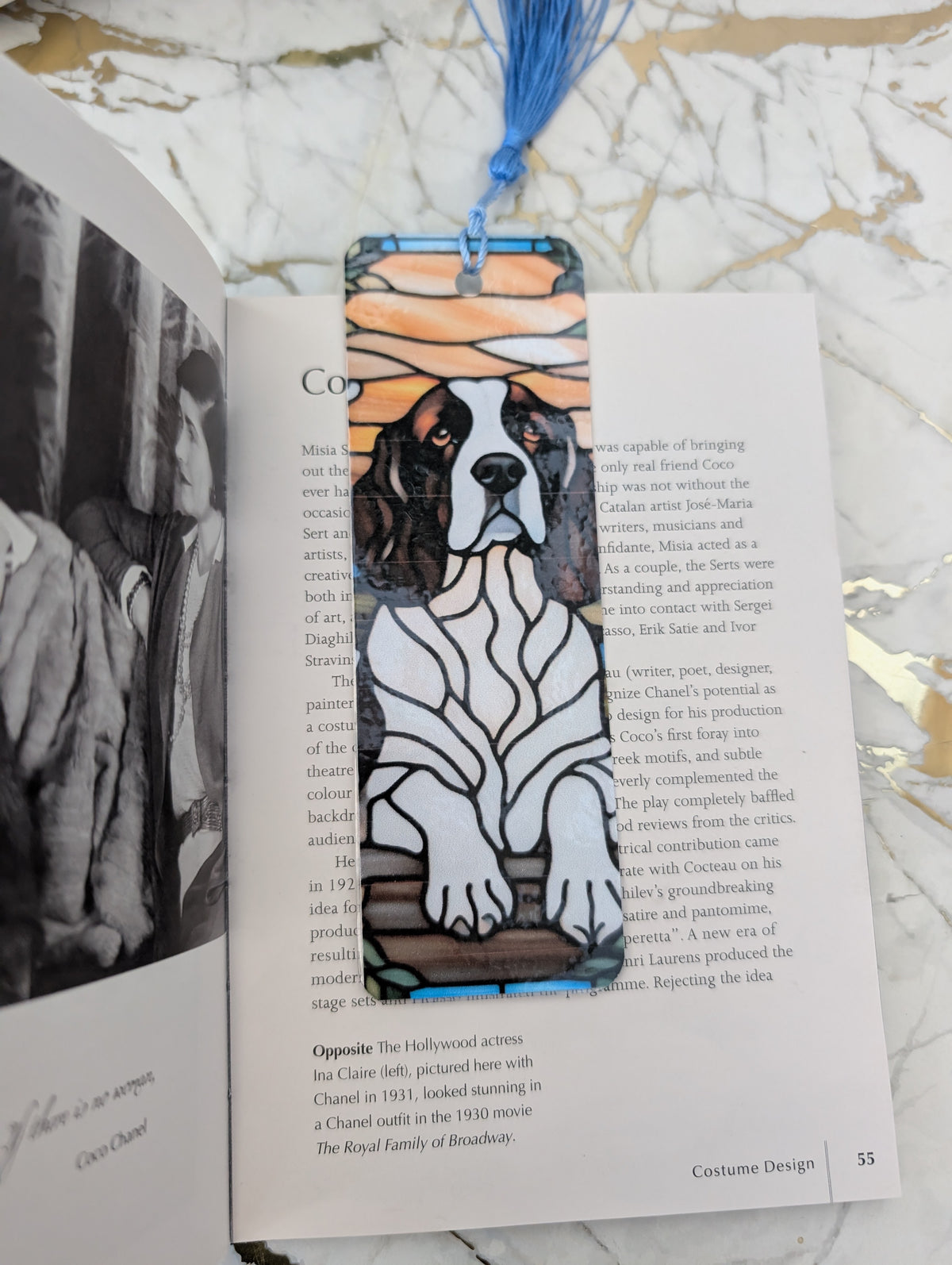 A rectangular book bookmark featuring a springer spaniel stained glass style illustration with a blue tassell, resting on an open book on a marble surface.