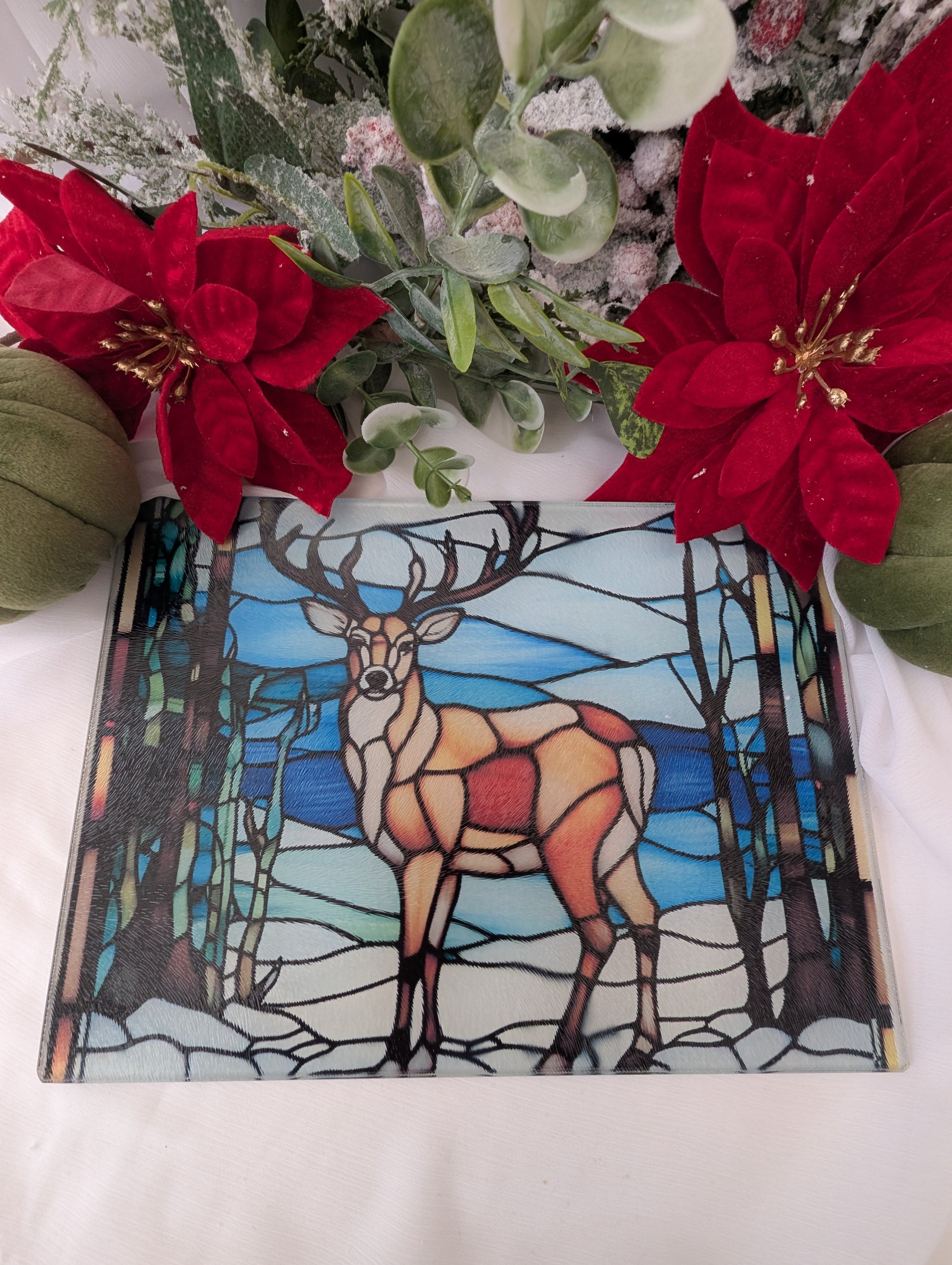 Stained glass chopping board with deer design next to red flowers on a white surface