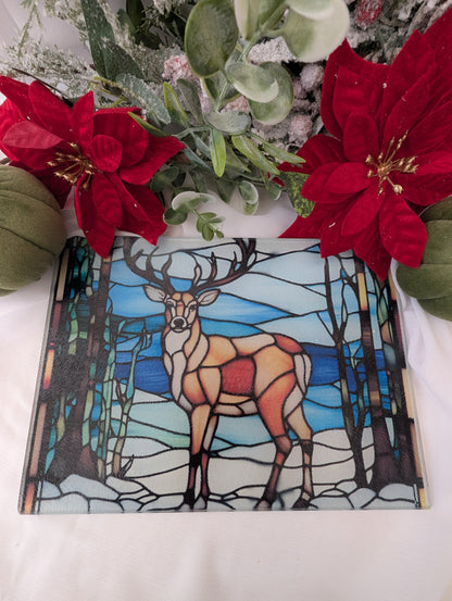 Stained glass chopping board with deer design next to red flowers on a white surface