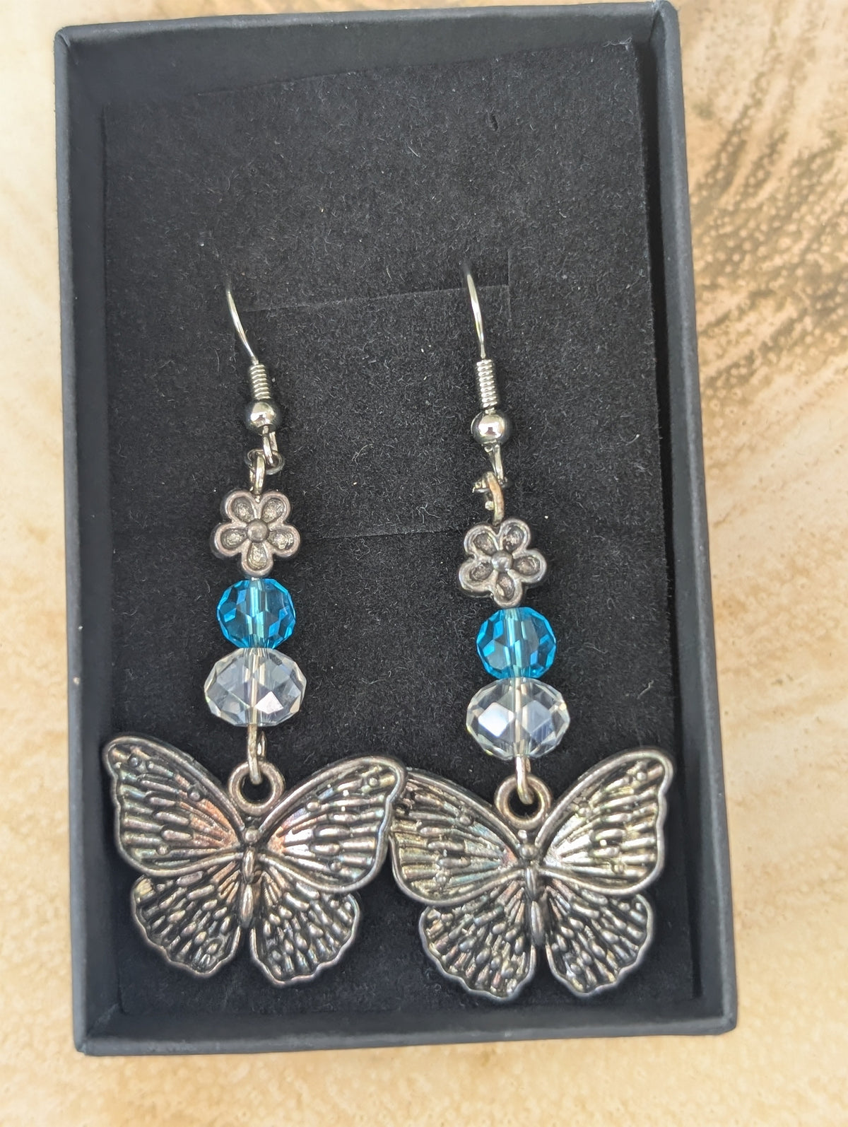 Butterfly earrings with blue and clear beads in a black box on a textured surface