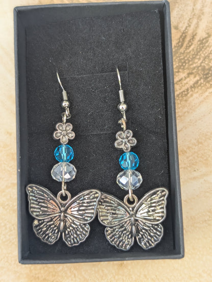 Butterfly earrings with blue and clear beads in a black box on a textured surface
