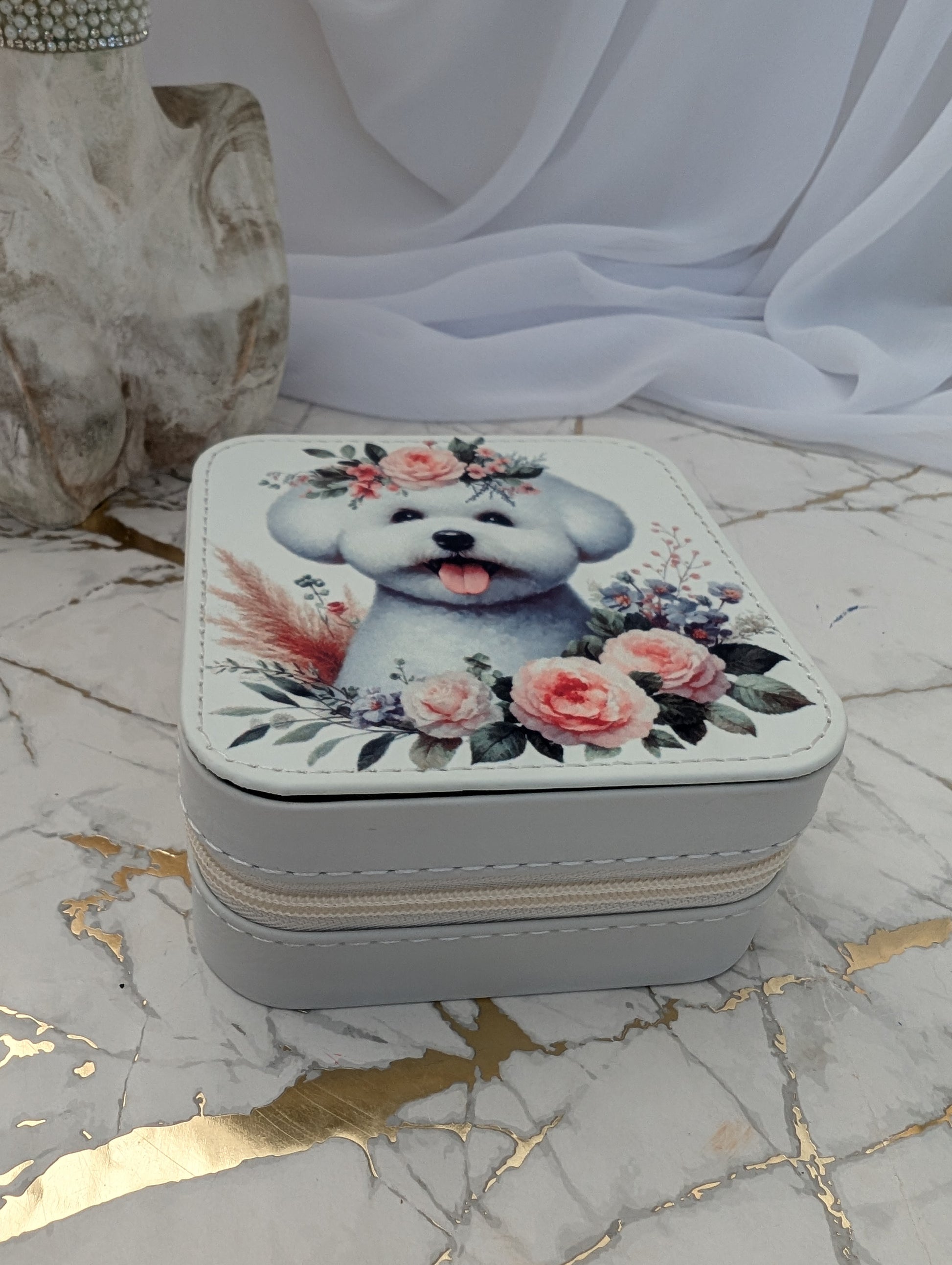 Small square jewelry box with a Bichon Frise and floral design on a marble surface.
