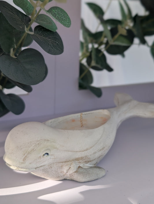 Decorative dolphin ornament on a white surface with green leaves in the background