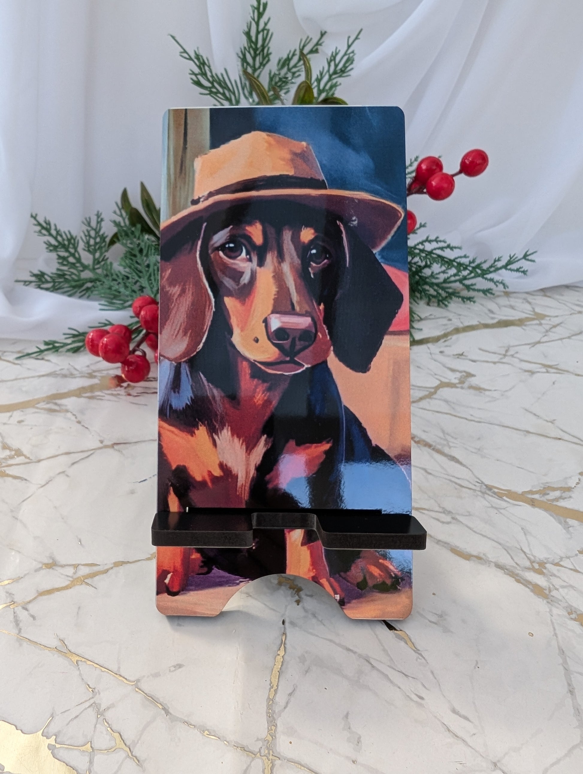 Phone stand with a dachshund wearing a trilby hat on a marble surface with greenery and berries.
