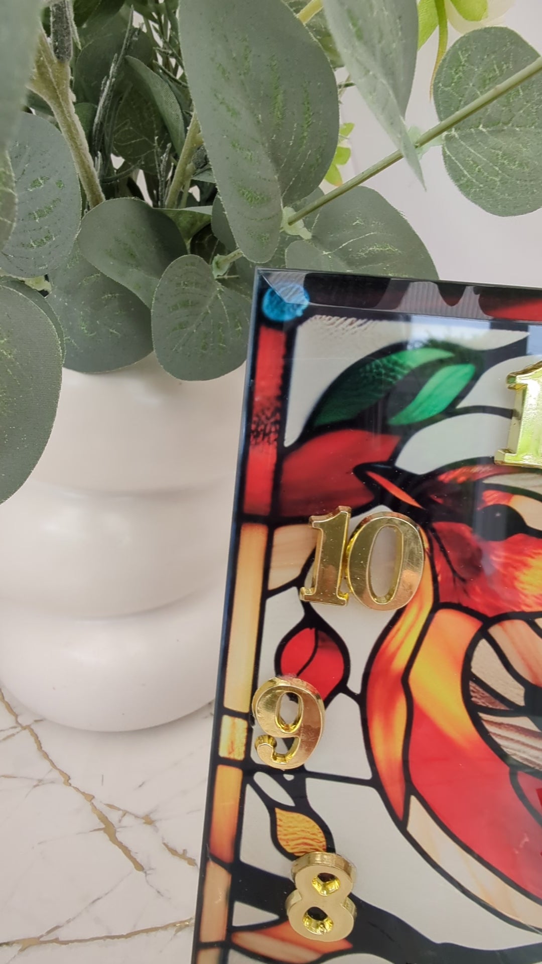 Video of robin clock turning slowly to show stained glass-style details and freestanding design.