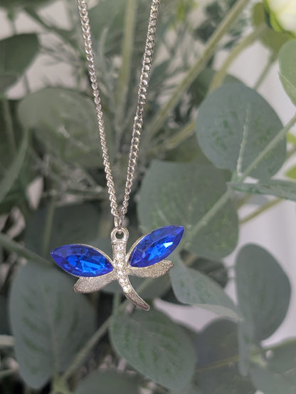 far shot of silver toned dragonfly pendant with sapphire blue colour crystal stone wings and clear diamante body accents